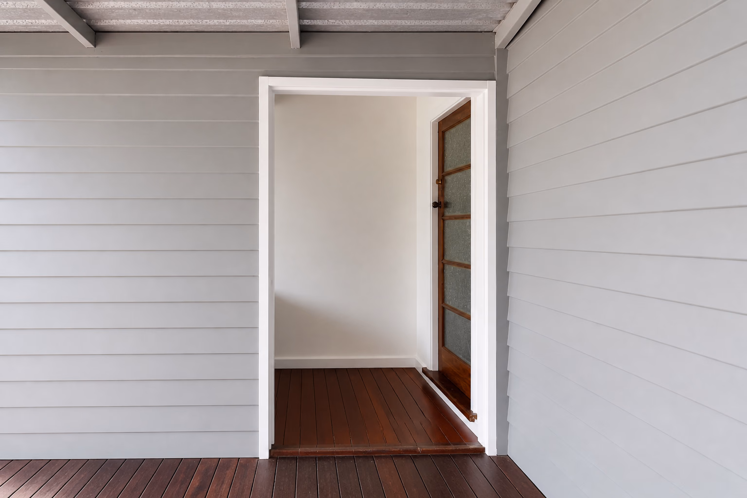 Grey weatherboard cladding around a white doorway onto a timber deck