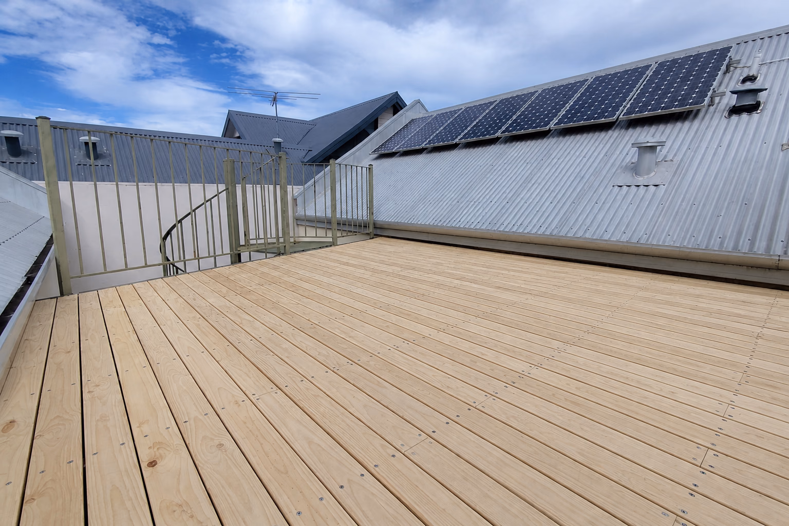 A light timber rooftop deck beside a metal roof and solar panels