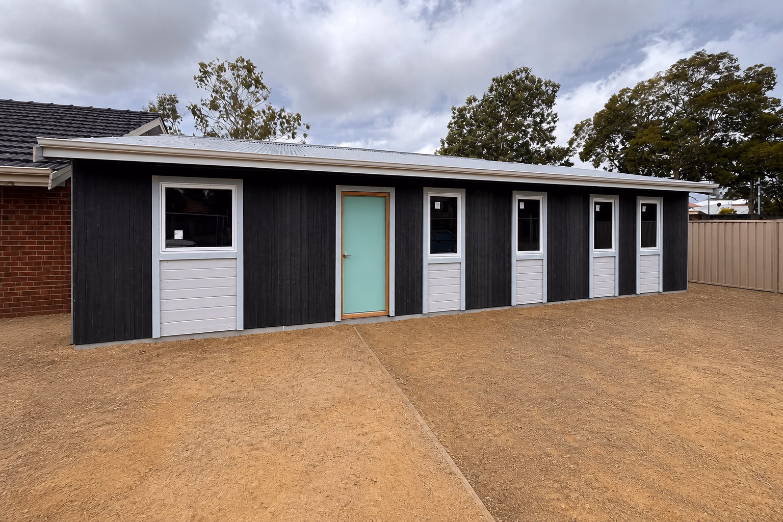 A dark vertical-clad granny flat with a mint door and white windows