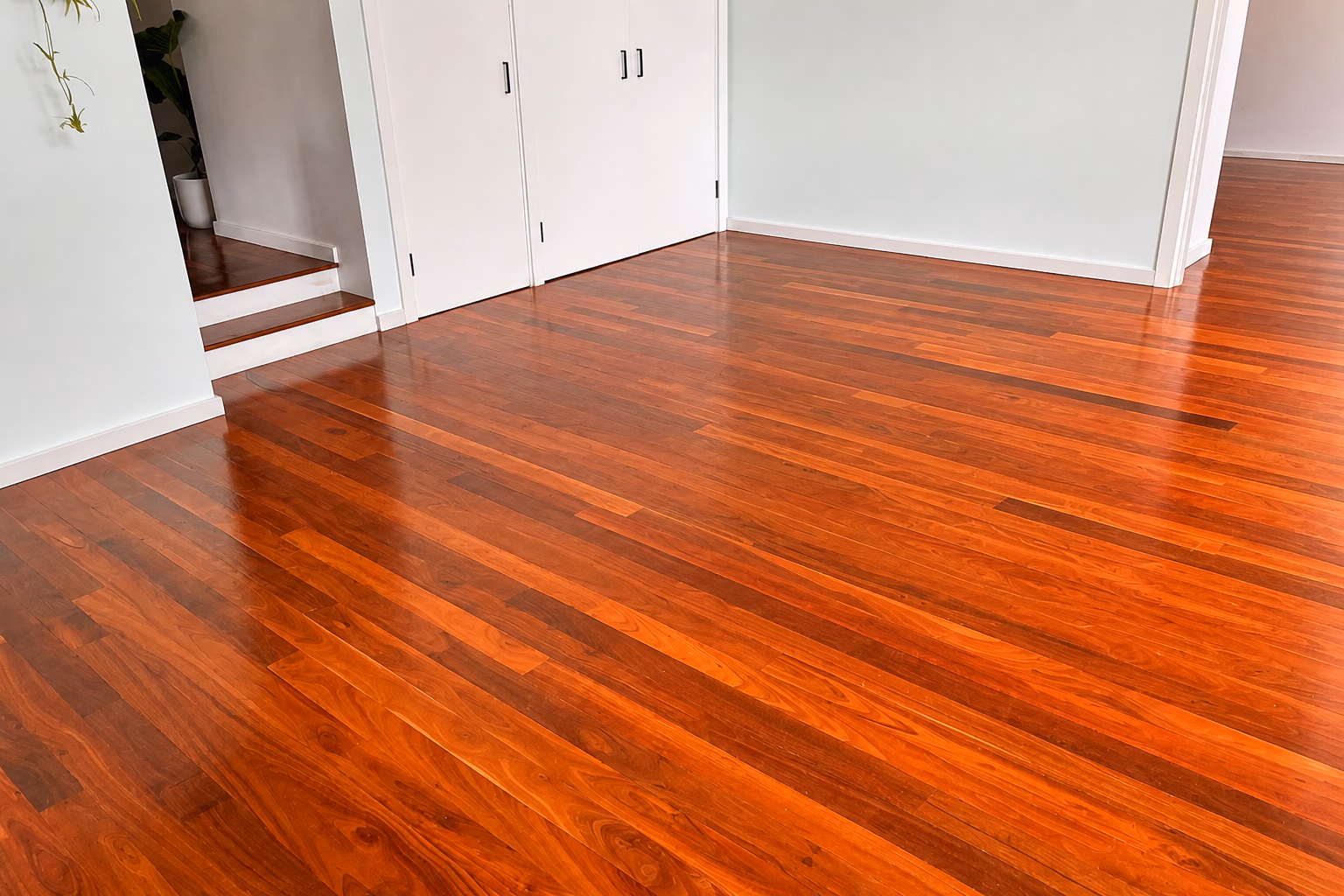 A polished hardwood floor in a room with white cabinets and timber stairs