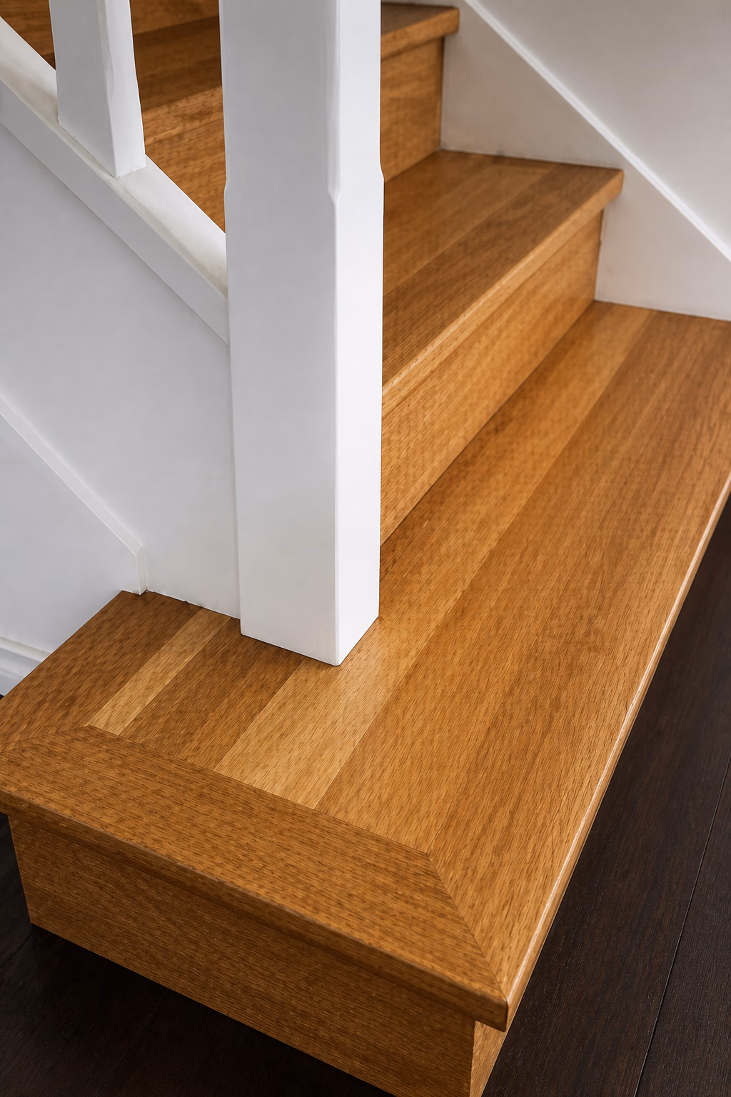 A mitered picture-frame hardwood stair tread beside a white newel